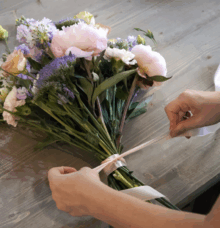 Händer som binder en bukett med blommor på ett träbord.