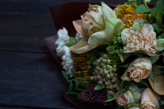En bukett med olika blommor, inklusive rosor och grönt lövverk, på ett mörkt bord.