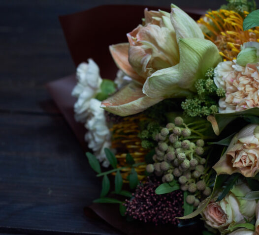 En bukett med olika blommor, inklusive rosor och grönt lövverk, på ett mörkt bord.